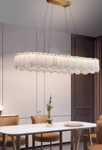 Long oval Aero chandelier lit above a white dining table, brass mounting bar visible on the ceiling