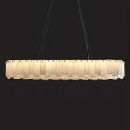 The long oval Aero chandelier lit against black, warm light escaping between its stacked stone panels