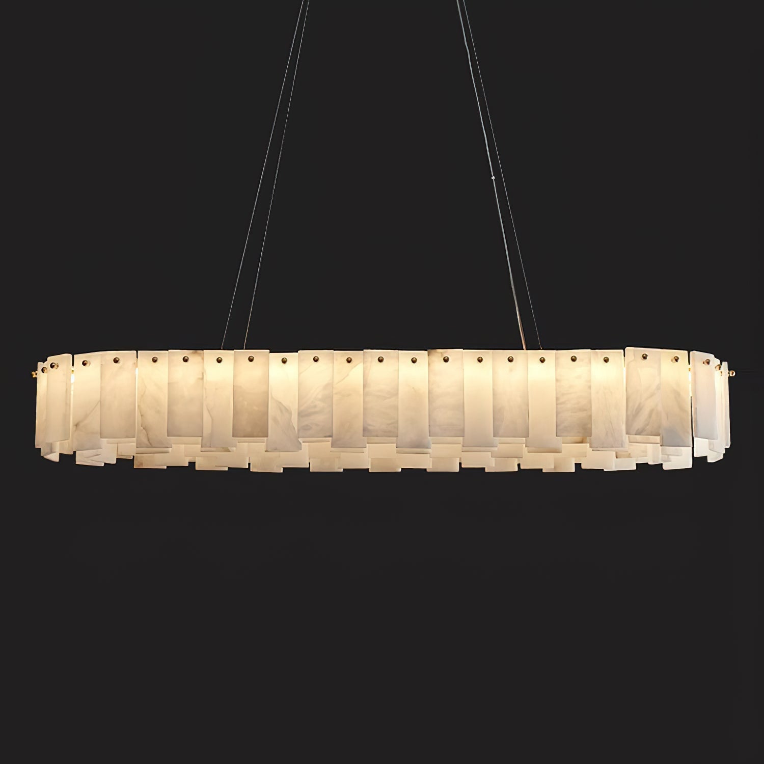 The long oval Aero chandelier lit against black, warm light escaping between its stacked stone panels