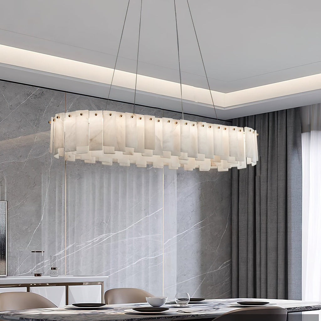 Long oval Aero chandelier lit over a set dining table in front of a grey marble wall
