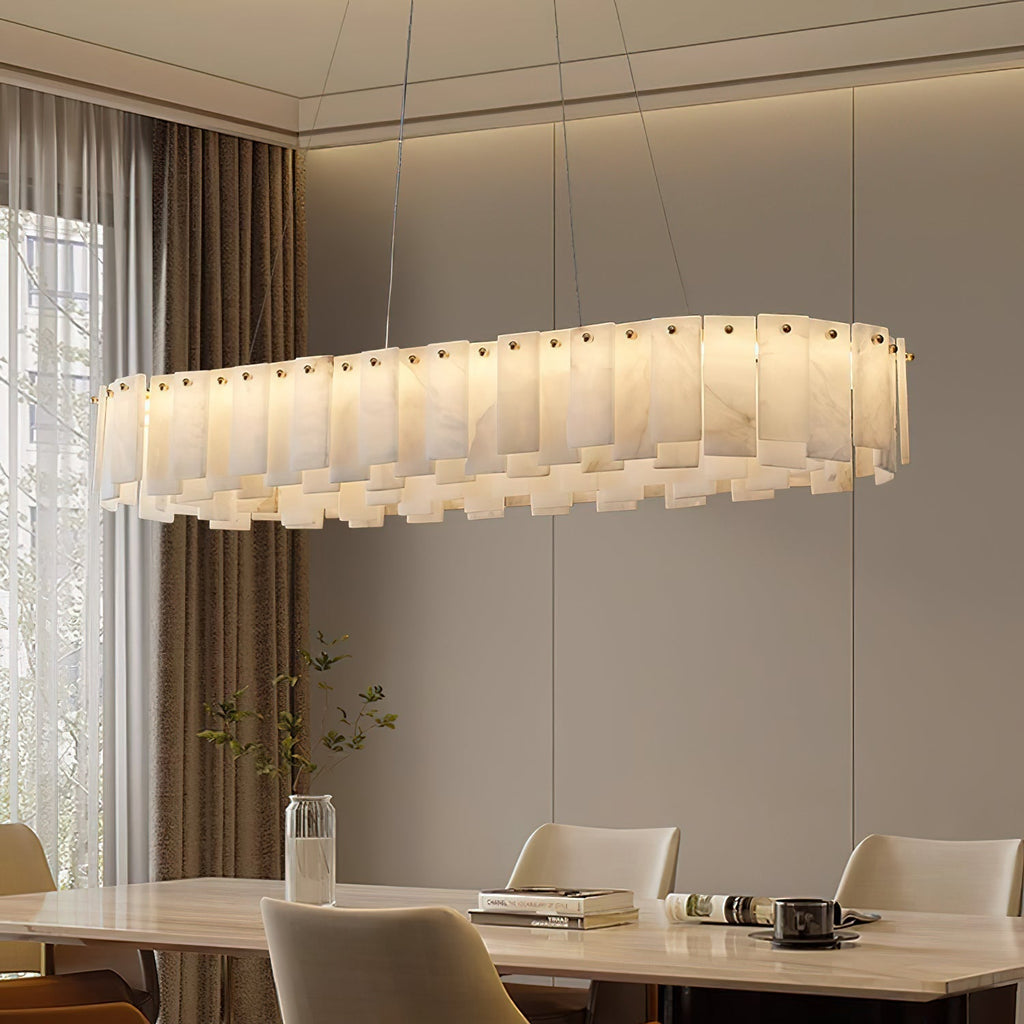 Long oval Aero chandelier lit above a wooden dining table beside floor-length curtains