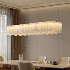 Long oval Aero chandelier lit above a wooden dining table beside floor-length curtains