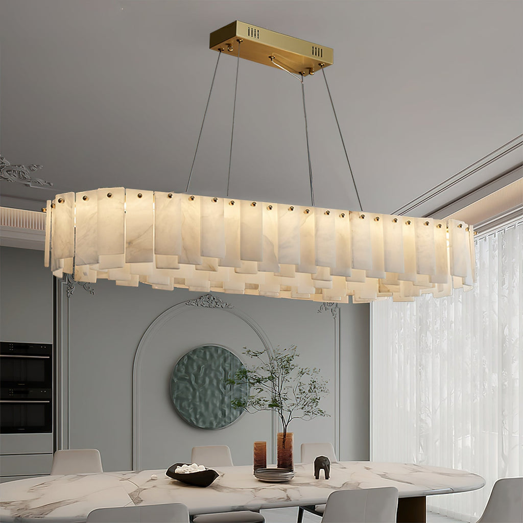 Aero chandelier's long oval form lit above a marble dining table, brass ceiling bar and cables in view