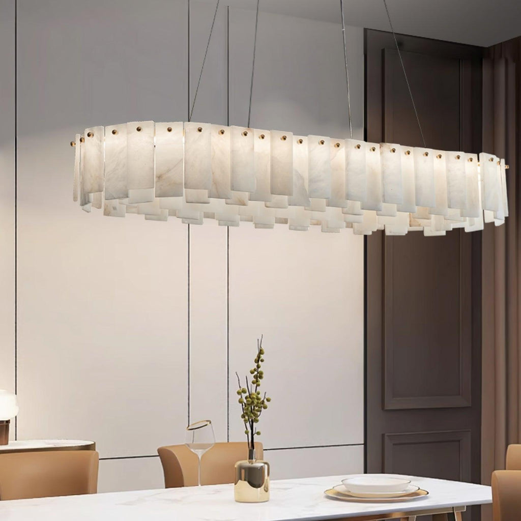 The long chandelier lit over a marble dining table beside a dark panelled door.