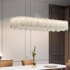 The long chandelier lit over a marble dining table beside a dark panelled door.