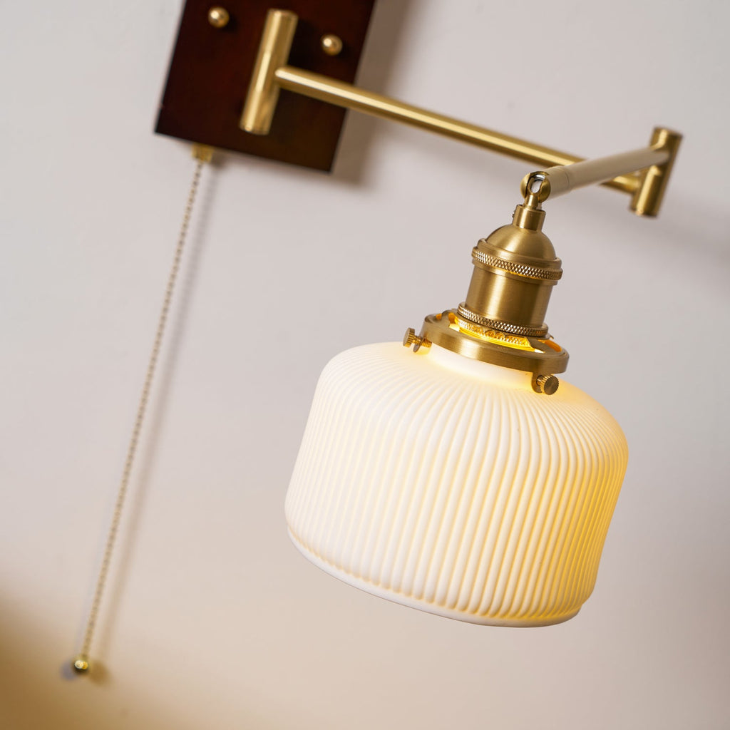 Ceramic wall lamp with walnut and brass detail glowing indoors