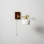 White ceramic wall lamp with brass arm lighting a quiet corner