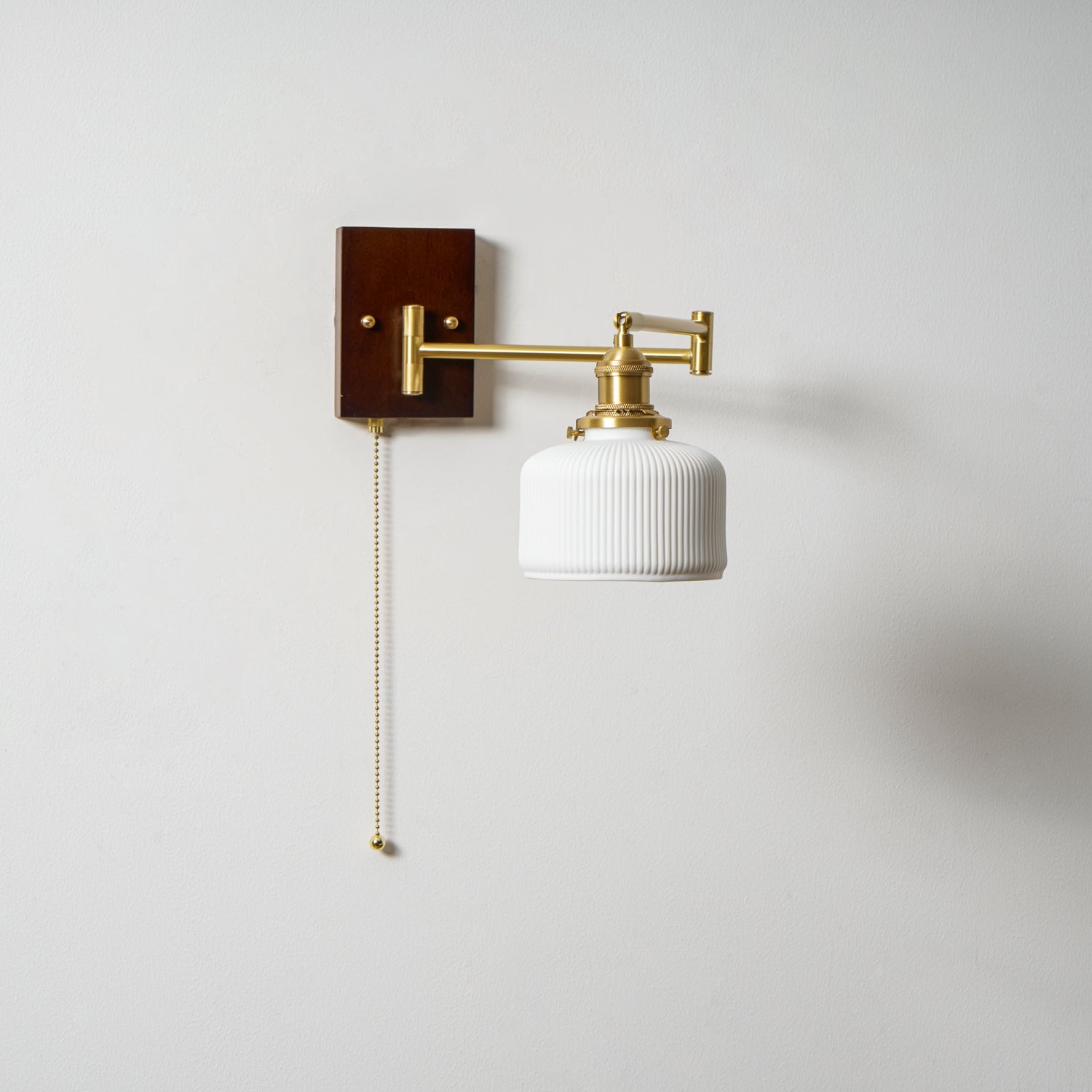 White ceramic wall lamp detail with brass fittings and walnut trim