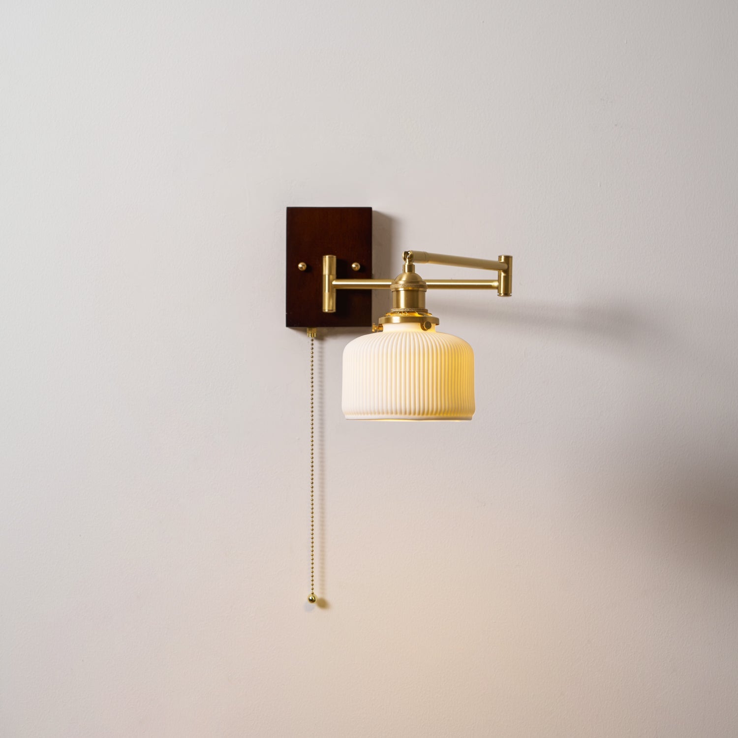 White ceramic wall lamp with pull chain mounted beside a bedside