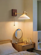 White ceramic wall lamp on walnut and brass beside a reading chair