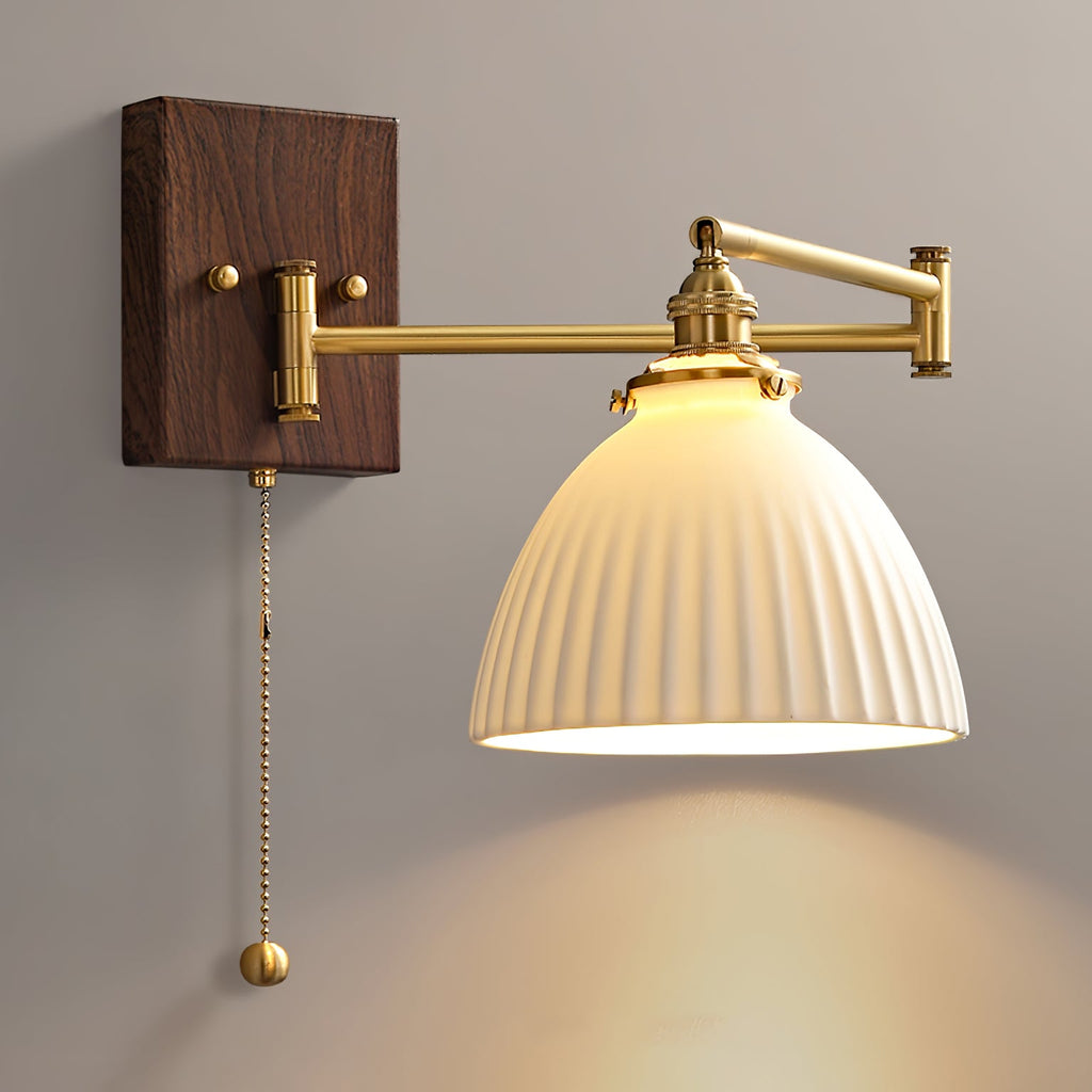 White ceramic wall lamp with pull chain lit warmly beside a bed