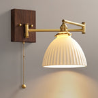 White ceramic wall lamp with pull chain lit warmly beside a bed