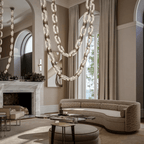 Chain-link chandelier draped past a fireplace and curved sofa in a high-ceilinged living room