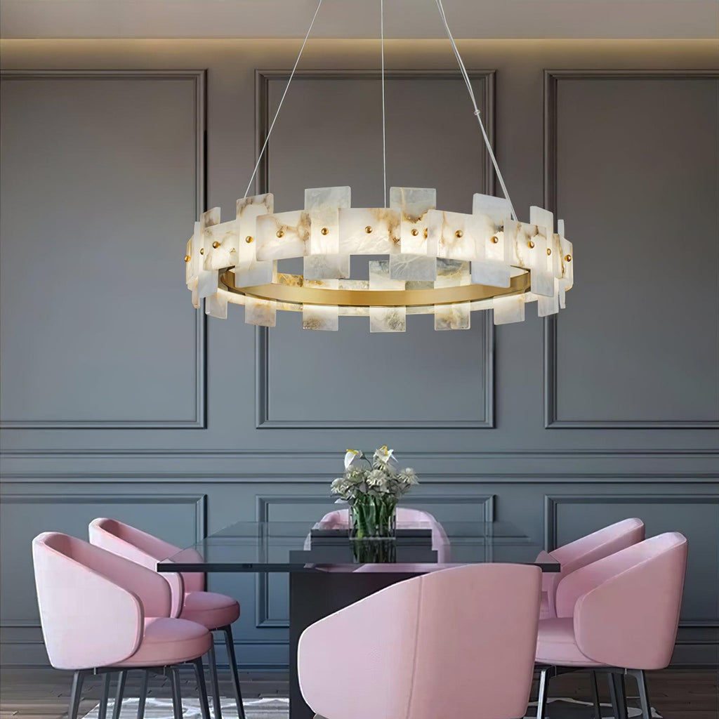 Lit above a glass dining table with pink velvet chairs, grey panelled walls behind.
