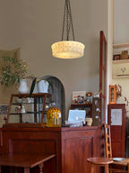 Above an antique wood counter set with jars and framed pictures, this beige fluted-glass Clérachic pendant hangs lit.