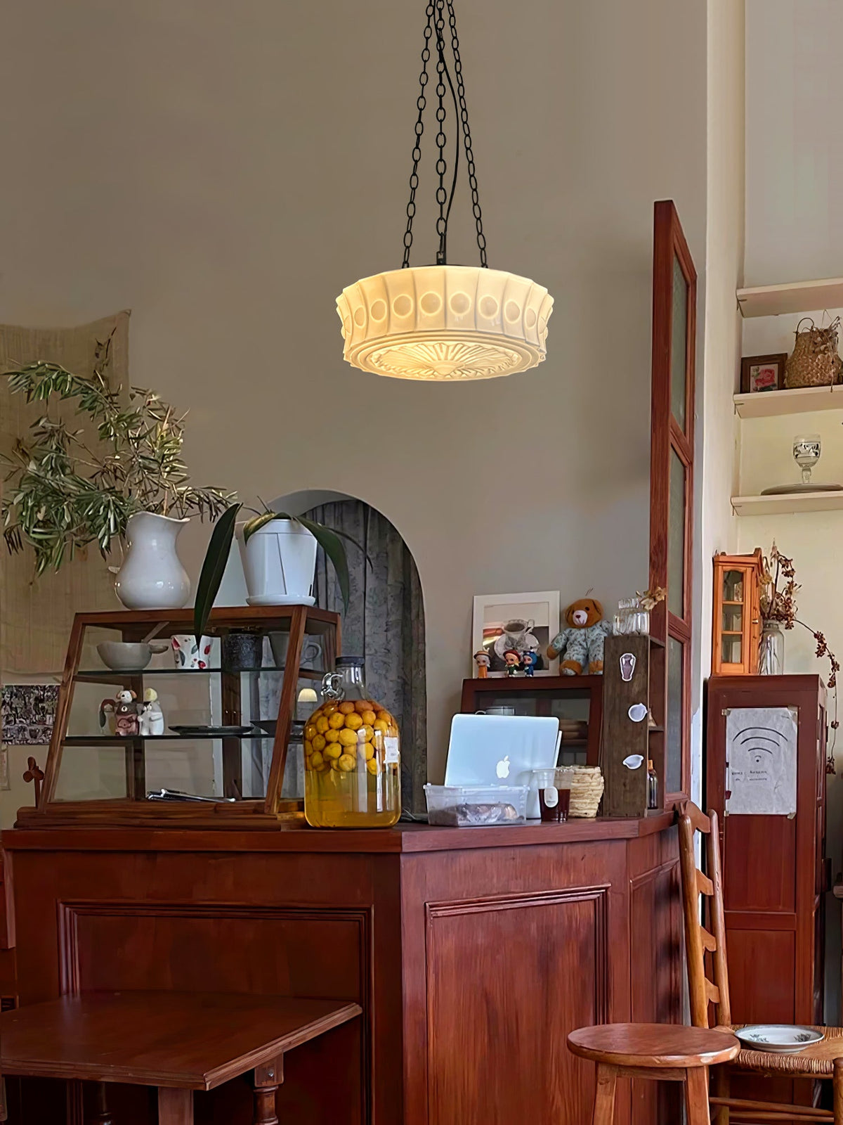 Above an antique wood counter set with jars and framed pictures, this beige fluted-glass Clérachic pendant hangs lit.