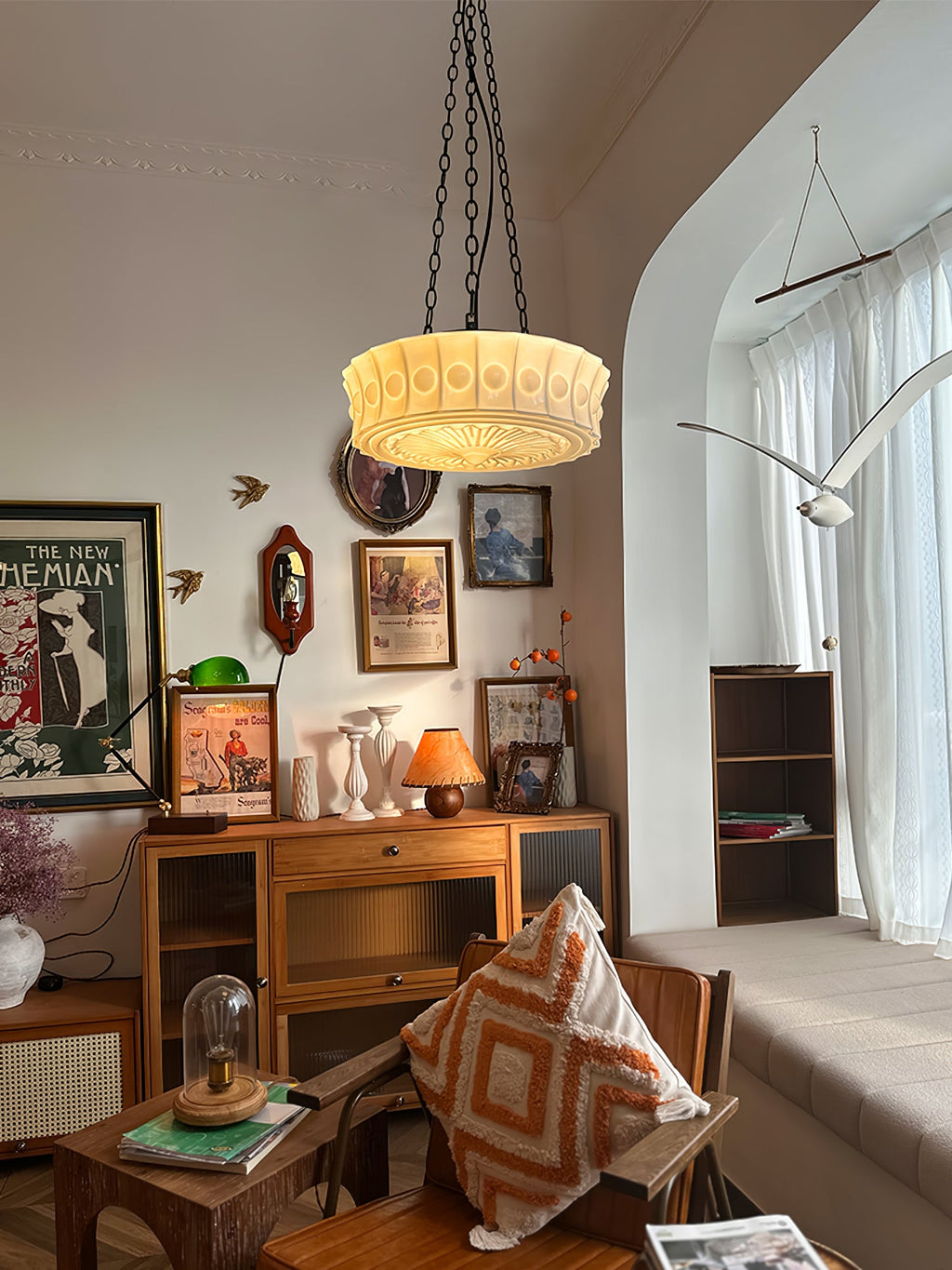 In an eclectic living room with a bookshelf and cushions, this beige fluted-glass Clérachic pendant glows near an arched doorway.