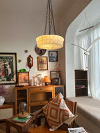 In an eclectic living room with a bookshelf and cushions, this beige fluted-glass Clérachic pendant glows near an arched doorway.