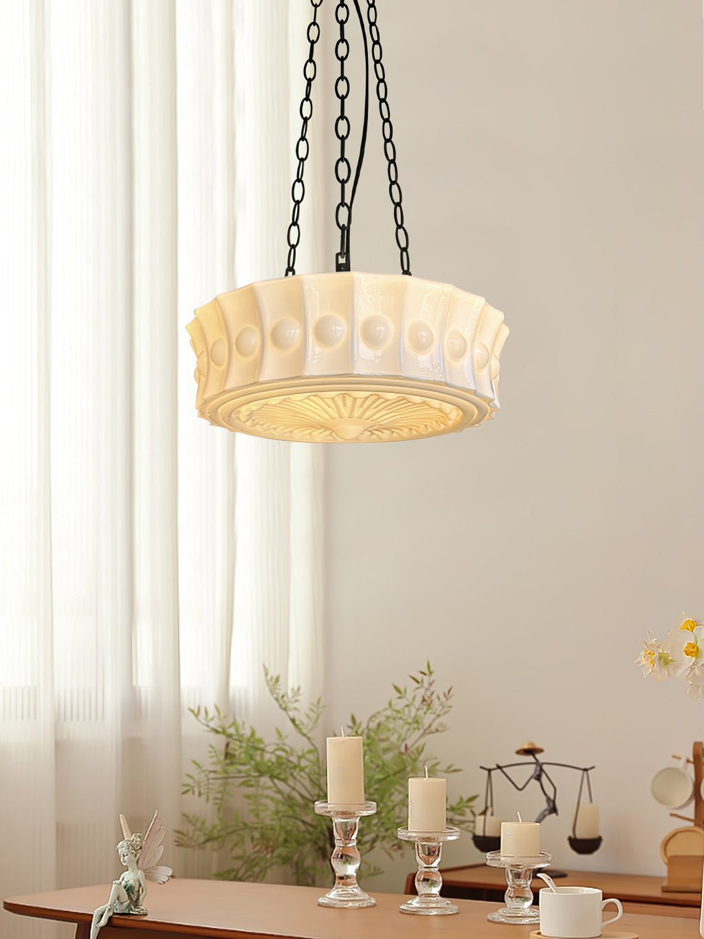 In front of a sheer curtain, this white fluted-glass Clérachic pendant hangs above a table set with candles and small ornaments.