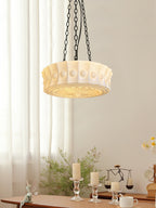 In front of a sheer curtain, this white fluted-glass Clérachic pendant hangs above a table set with candles and small ornaments.