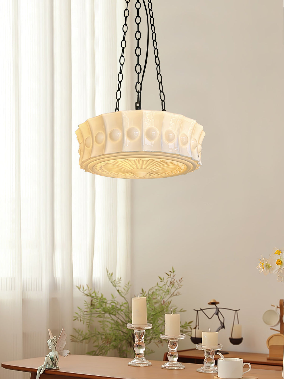 In front of a sheer curtain, this white fluted-glass Clérachic pendant hangs above a table set with candles and small ornaments.
