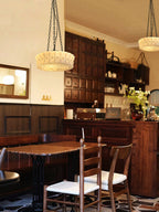 Two beige fluted-glass Clérachic pendants hang in a rustic kitchen with dark wood cabinetry and a table set for dining.