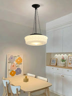 Above a small round dining table with white chairs and colourful wall art, this beige fluted-glass Clérachic pendant glows.