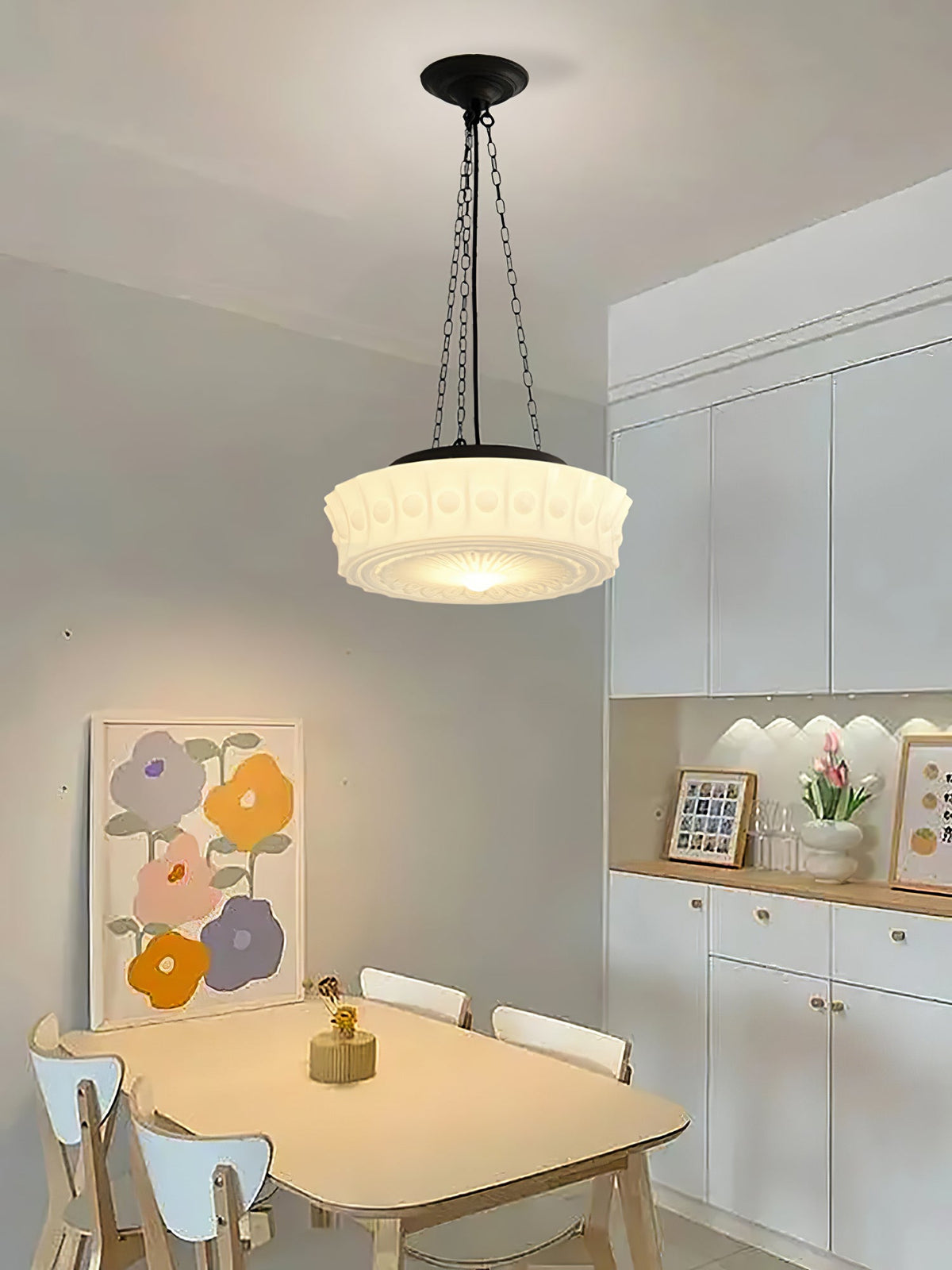 Above a small round dining table with white chairs and colourful wall art, this beige fluted-glass Clérachic pendant glows.