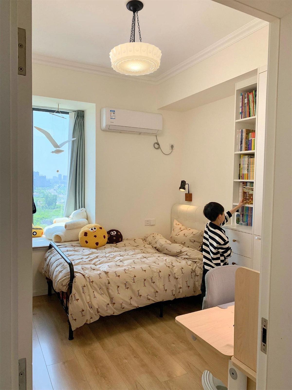 Seen through a doorway, this beige fluted-glass Clérachic pendant hangs above a child's bed and a bookshelf.