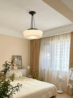 In a bedroom with sheer and gold curtains, this beige fluted-glass Clérachic pendant glows beside a floor fan.
