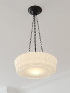 A close view of this white fluted-glass Clérachic pendant glowing softly beneath crown moulding on a plain wall.