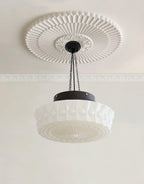 Beneath a large ribbed ceiling medallion, this beige fluted-glass Clérachic pendant's chains meet a black canopy.