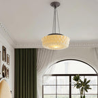Under an arched ceiling with crown moulding, this beige fluted-glass Clérachic pendant hangs beside a green curtain and a potted plant.