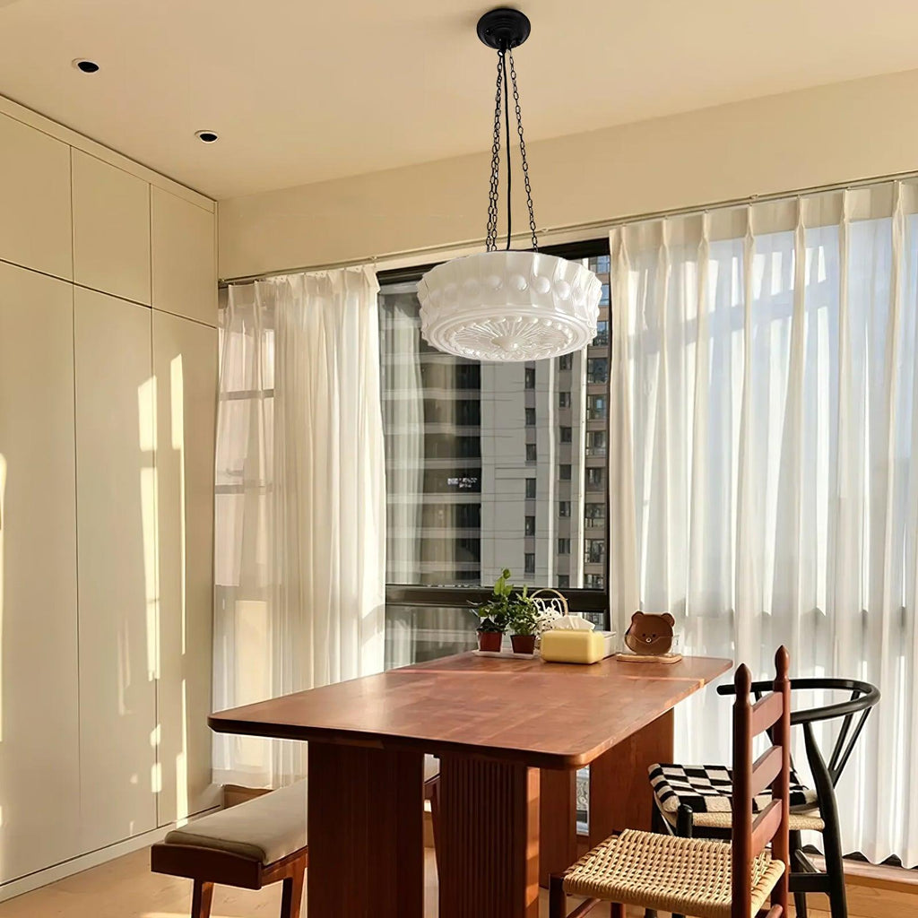 Beside sheer curtains with a city view outside, this beige fluted-glass Clérachic pendant hangs above a wood dining table.