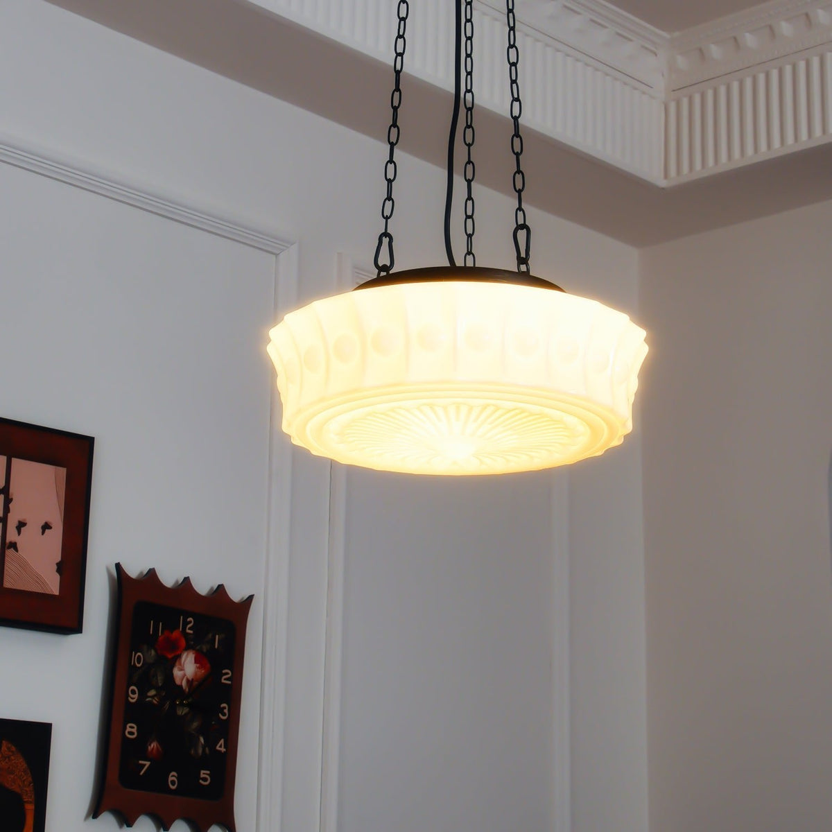 Near a gallery wall of framed clock-face artworks, this beige fluted-glass Clérachic pendant hangs beneath ceiling crown moulding.