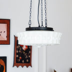 Near a gallery wall of framed pictures, one in a red frame, this white fluted-glass Clérachic pendant hangs lit.