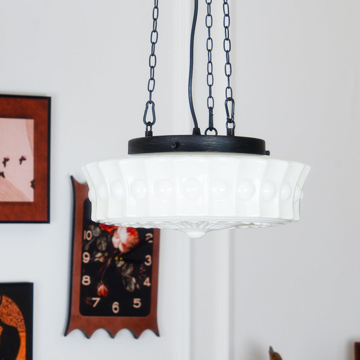 Near a gallery wall of framed pictures, one in a red frame, this white fluted-glass Clérachic pendant hangs lit.