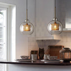 Glass pendant light with slim stem lit softly against a wall