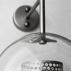 Glass globe wall light with slim stem lit softly in a room