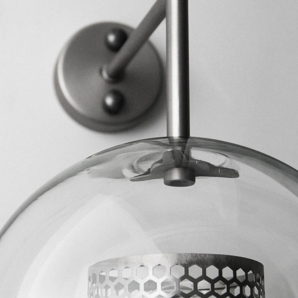 Glass globe wall light with slim stem lit softly in a room