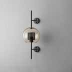 Glass wall light with slim metal stem lit softly beside a wall