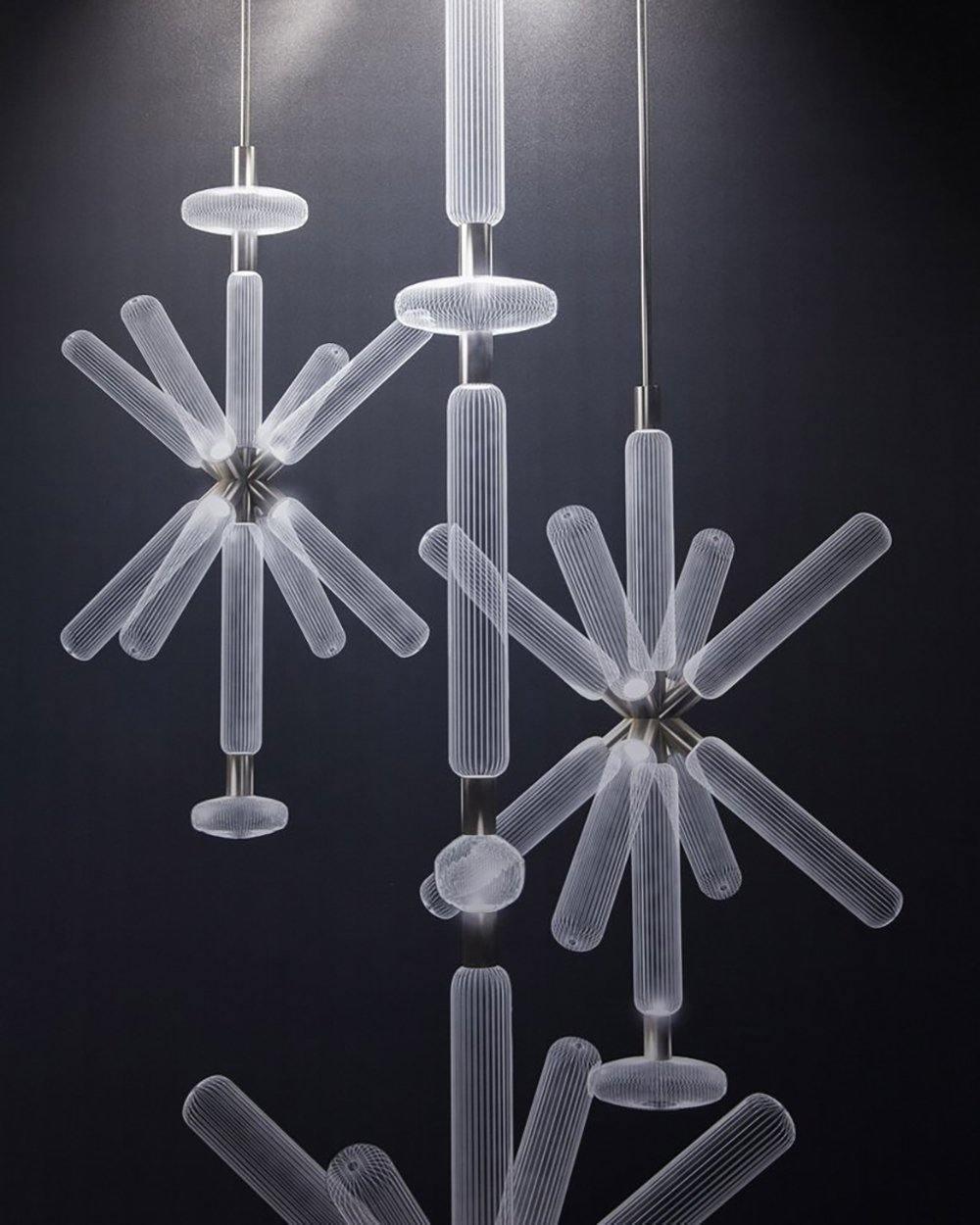 Three Clérachic pendants cluster together, unlit, their crystal rods layered against a dark wall.