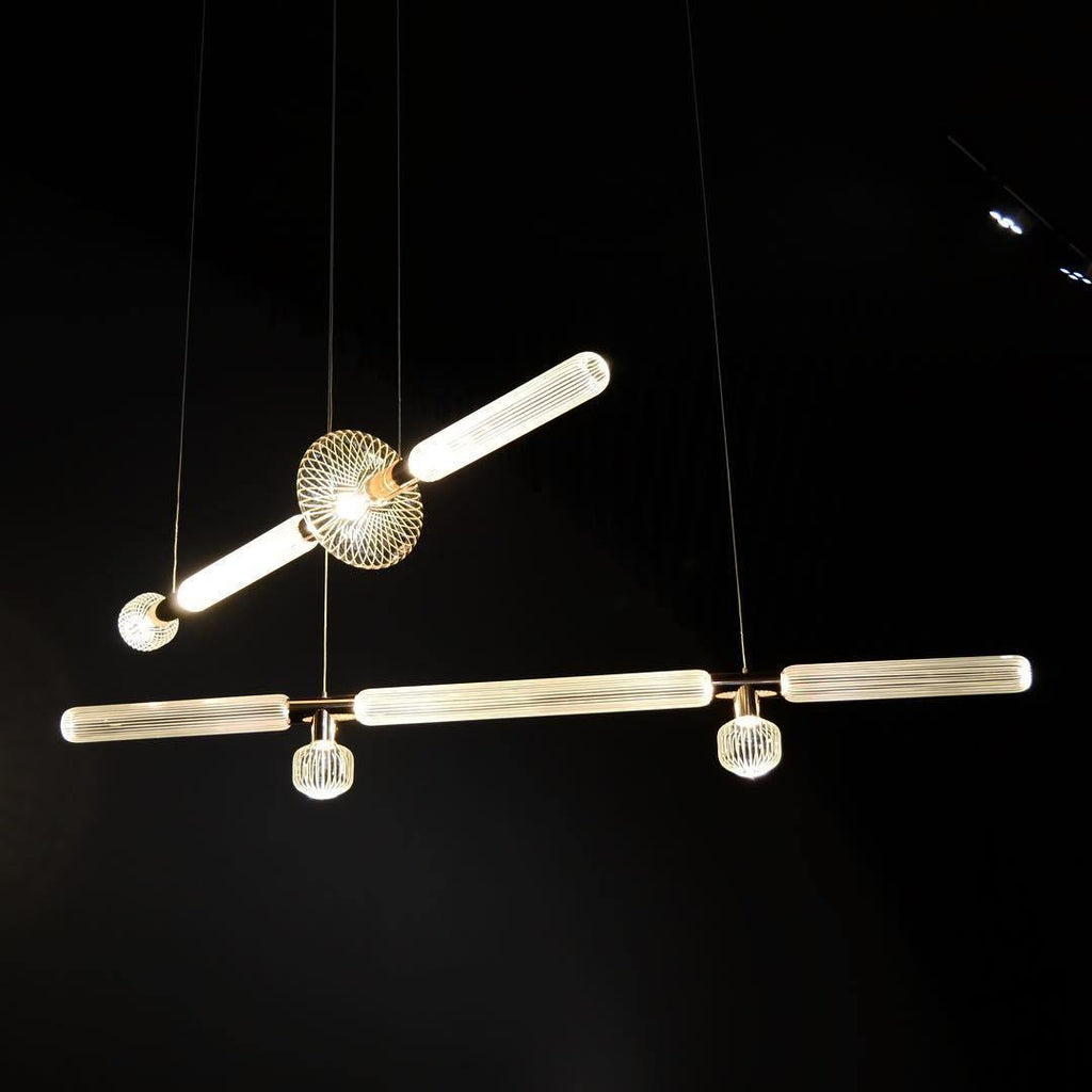Two linear Clérachic pendants cross near a round gold joint, lit against a black backdrop.
