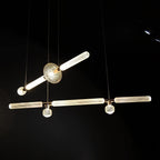 Two linear Clérachic pendants cross near a round gold joint, lit against a black backdrop.