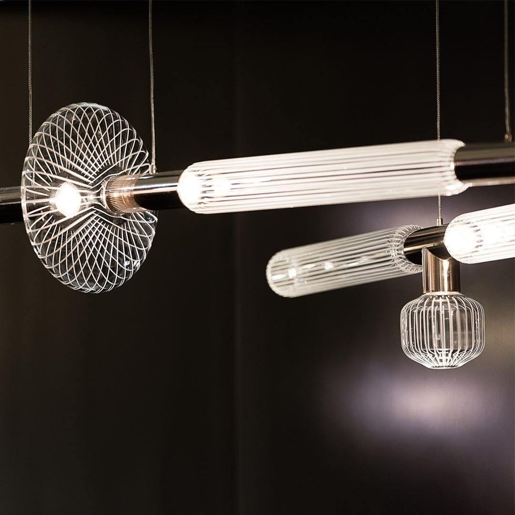 A horizontal Clérachic pendant with fluted glass cylinders hangs flanked by wire-cage fixtures of a different design.