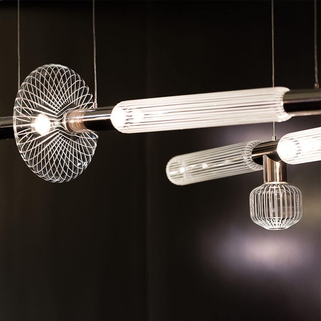 A horizontal Clérachic pendant with fluted glass cylinders hangs flanked by wire-cage fixtures of a different design.