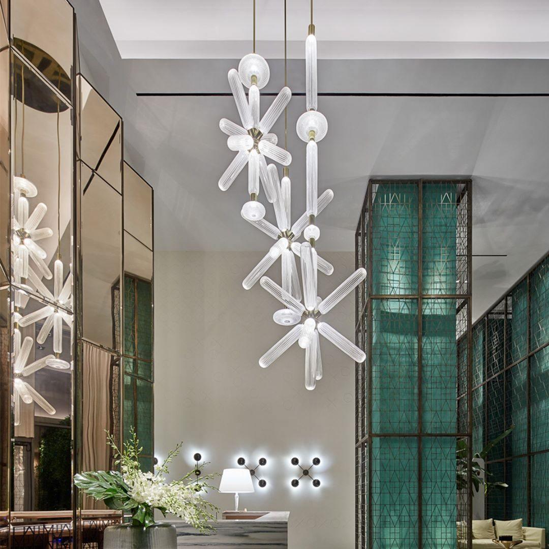 Two Clérachic pendants at different heights glow beside green glass panels in a lobby setting.