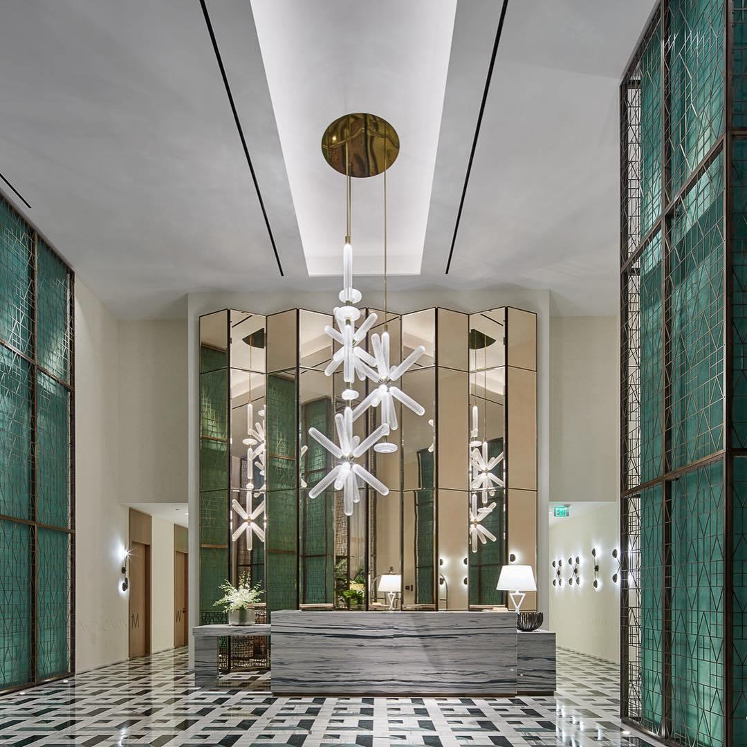 This Clérachic pendant hangs lit in a hotel corridor, reflected in mirrored panels above a stone console.
