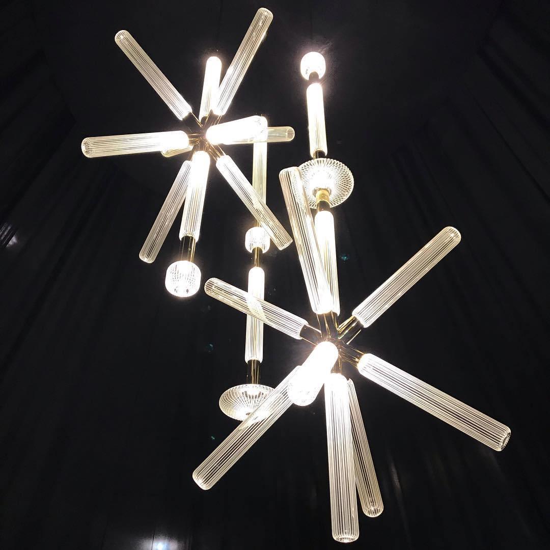 This Clérachic pendant's crystal rods glow warmly, clustered together against a black backdrop.
