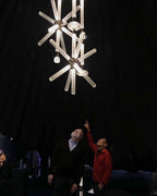 People look up at a lit Clérachic pendant cluster hanging high overhead in a dark venue.